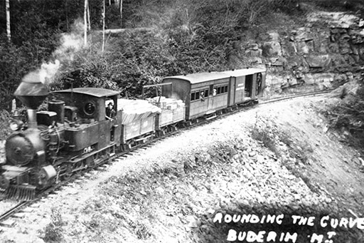 A black and white photo showing a steam-powered locomotive rounding a curve.