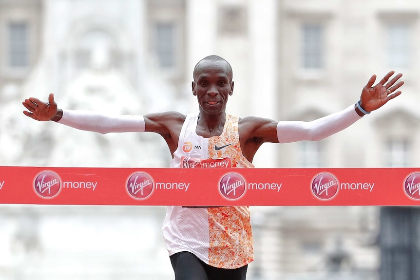 Eliud Kipchoge holds his arms wide as he runs towards a red tape