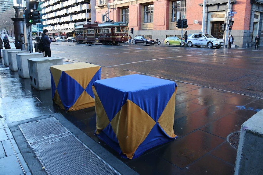 Blue and yellow triangle covers adorn two of the concrete security bollards outside Southern Cross Station.