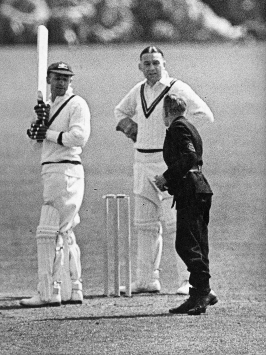 A man hands a note to another man while playing cricket.