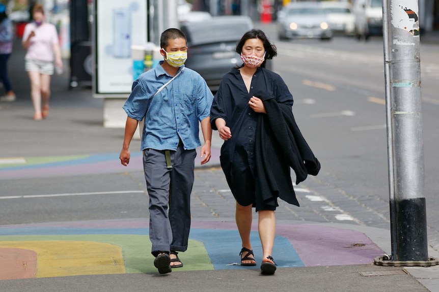 A man and a woman wearing face masks walk on a Melbourne street.