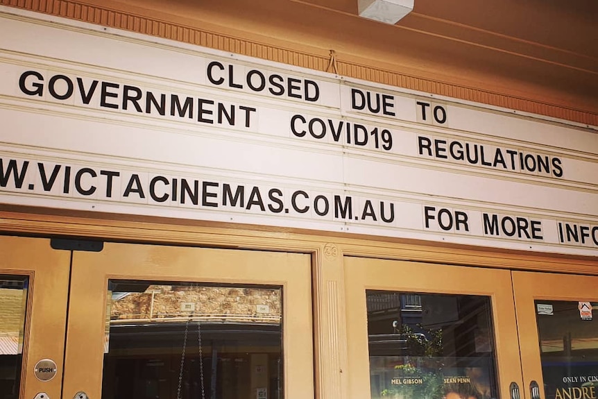 A sign that says 'closed due to COVID-19 regulations on the front door of a cinema