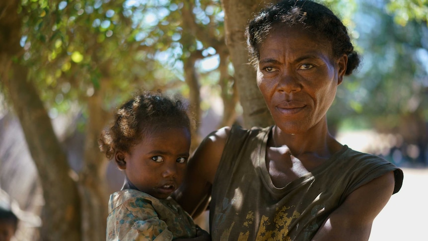 Julienne holding her daughter with trees out of focus in the background.