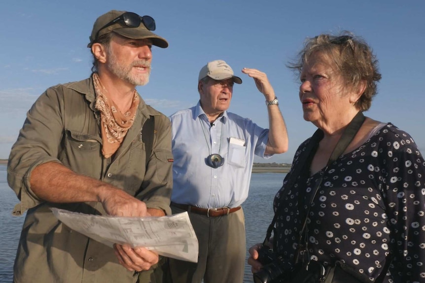 Three middle-aged people at the coast talking to one another