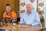Two men sitting next to one another, smiling during a press conference 