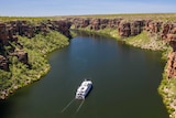 Image of a boat travelling up a river in a gorge with bushland on either side.