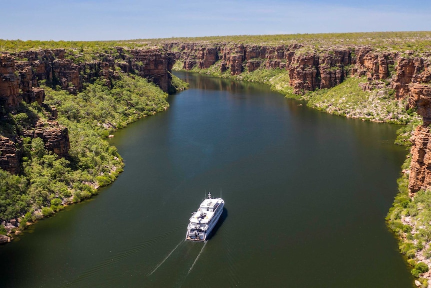 Image of a boat travelling up a river in a gorge with bushland on either side.