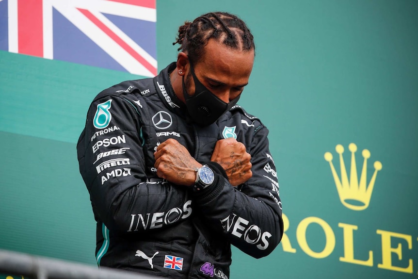 Hamilton stands on the podium with his head bowed and arms folded across his chest