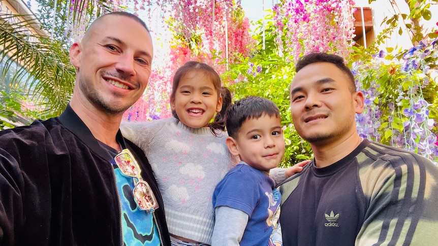Two young men are holding two children under flowers