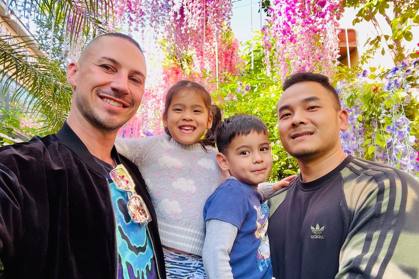 Two young men are holding two children under flowers