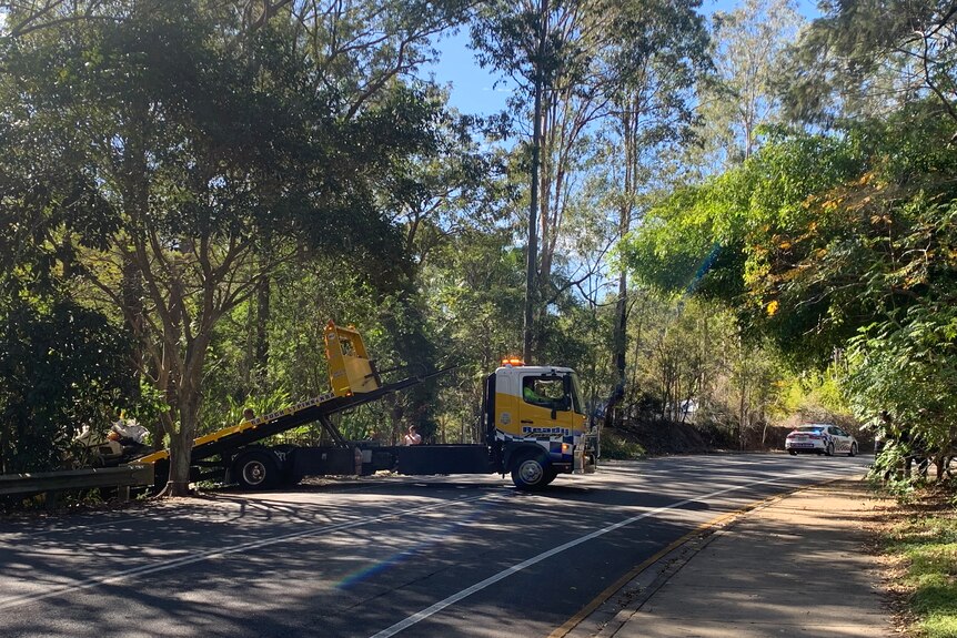 A tow truck on a road surrounded by trees.
