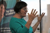 Cathy McGowan wears a teal coloured shirt while gesturing with her hands 