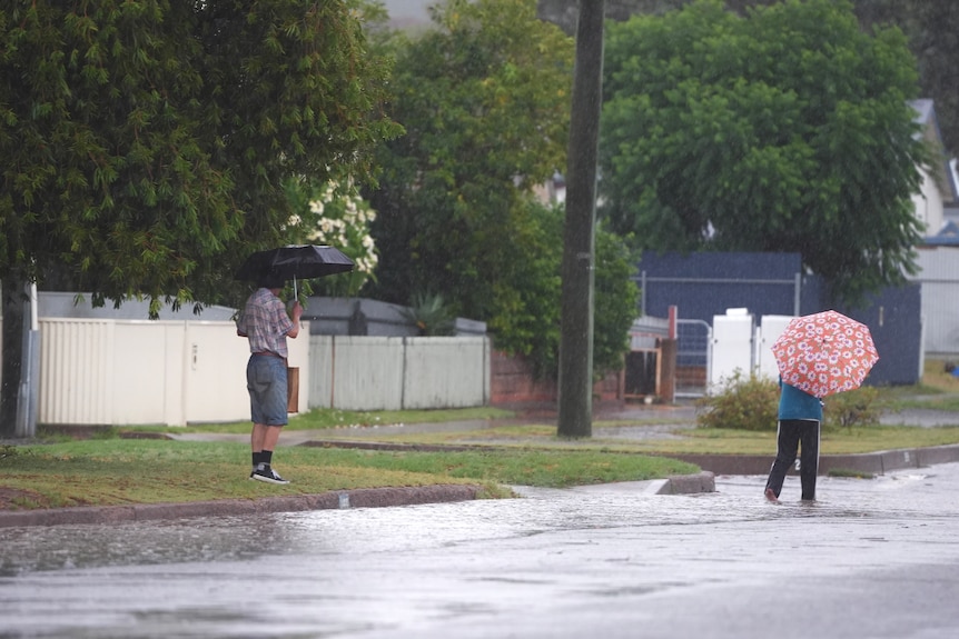 A man with an umbrella watches a woman walking along a rainy street in an outback city.