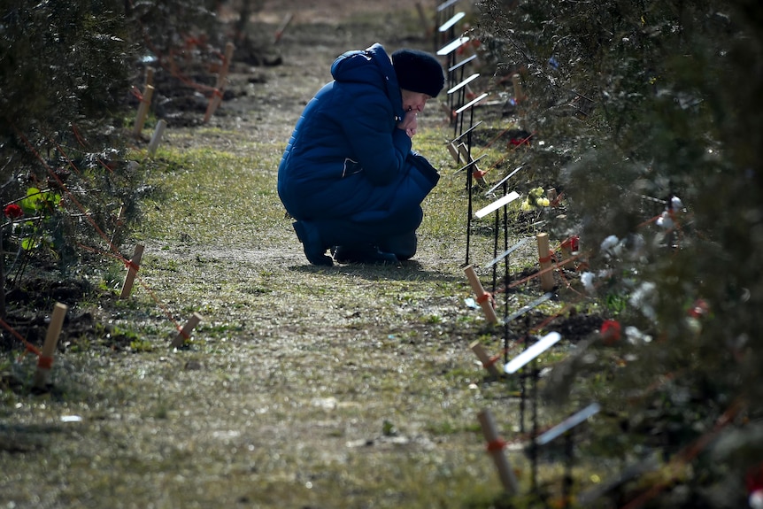 The mother of a Russian soldier who was killed in a military action in Ukraine, kneels near a planted tree in memory of her son.