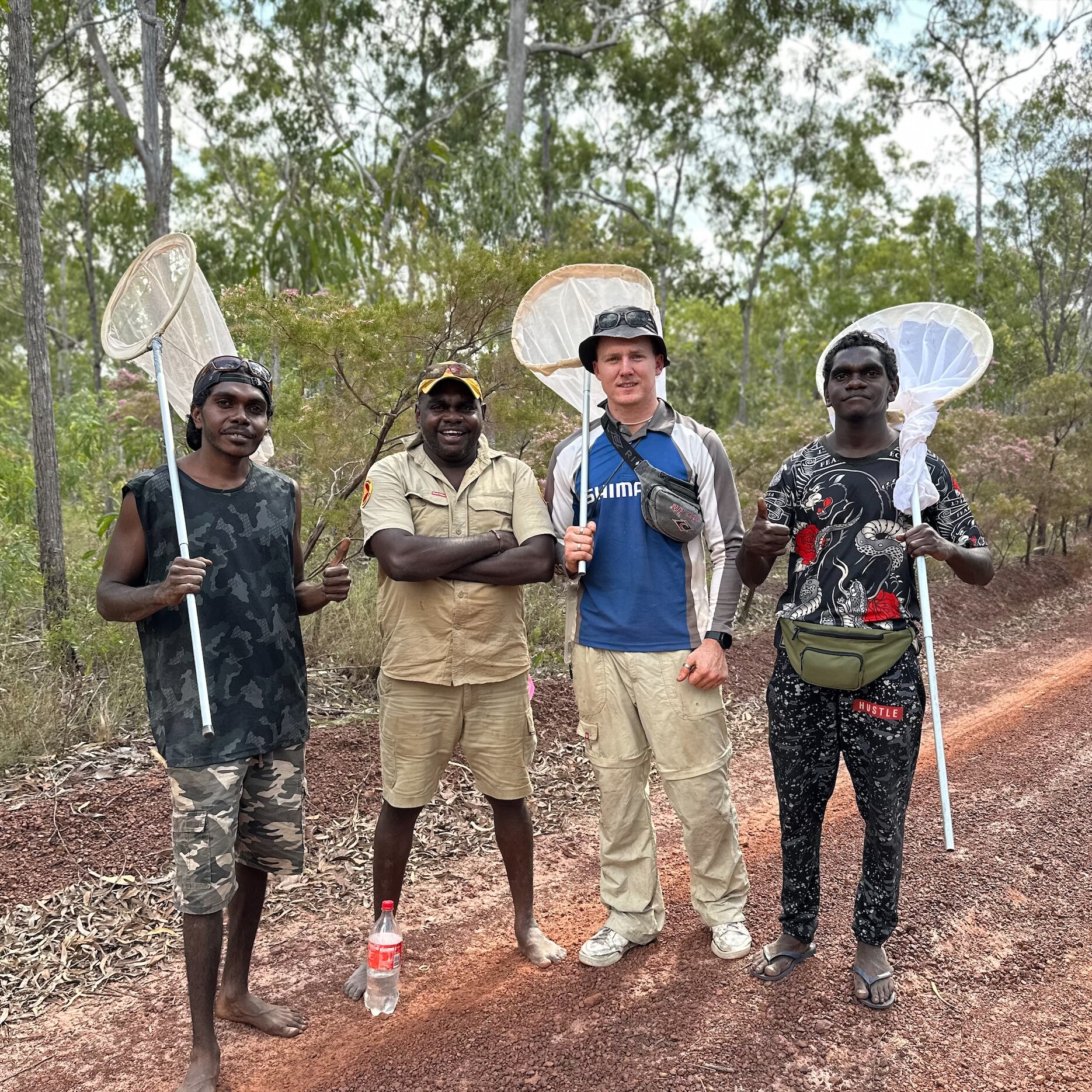 A photo of Clancy Lester holding a net. He's standing alongside three Indigenous rangers who are also holding nets.