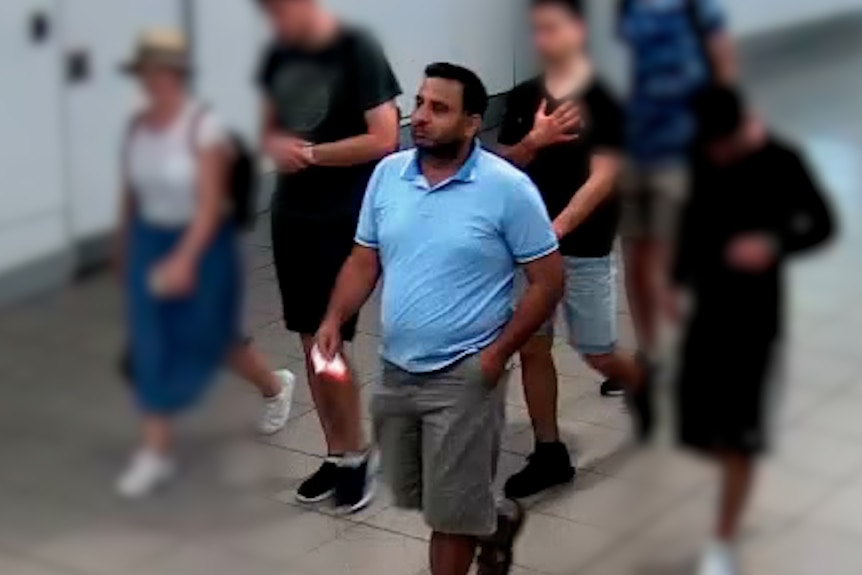 A man in shorts and a polo shirt walks through an airport terminal.