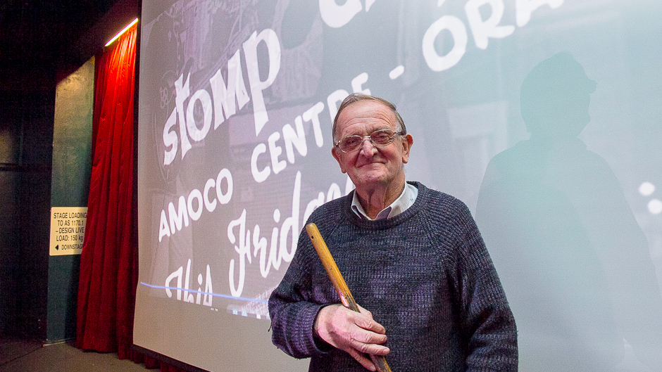A man standing with a broom in front of a screen with the words Stomp City, Amoco Centre
