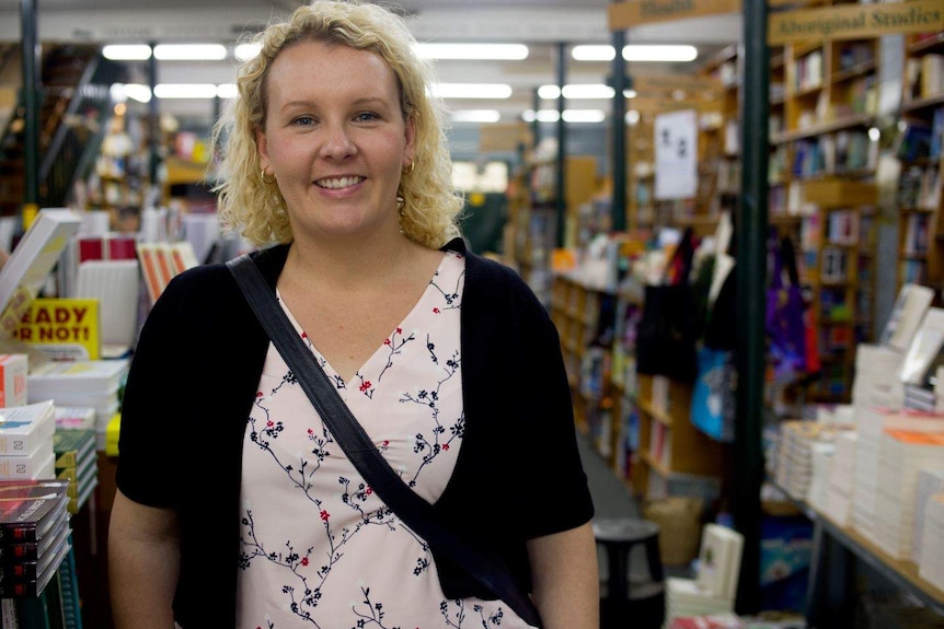 A woman stands in a book shop smiling to camera