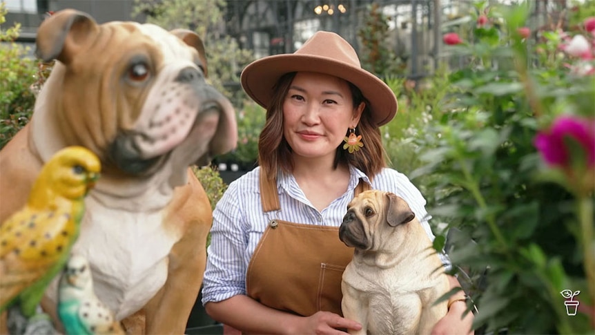 Tammy in a gardenwith statues of pet dogs and a budgerigar. 