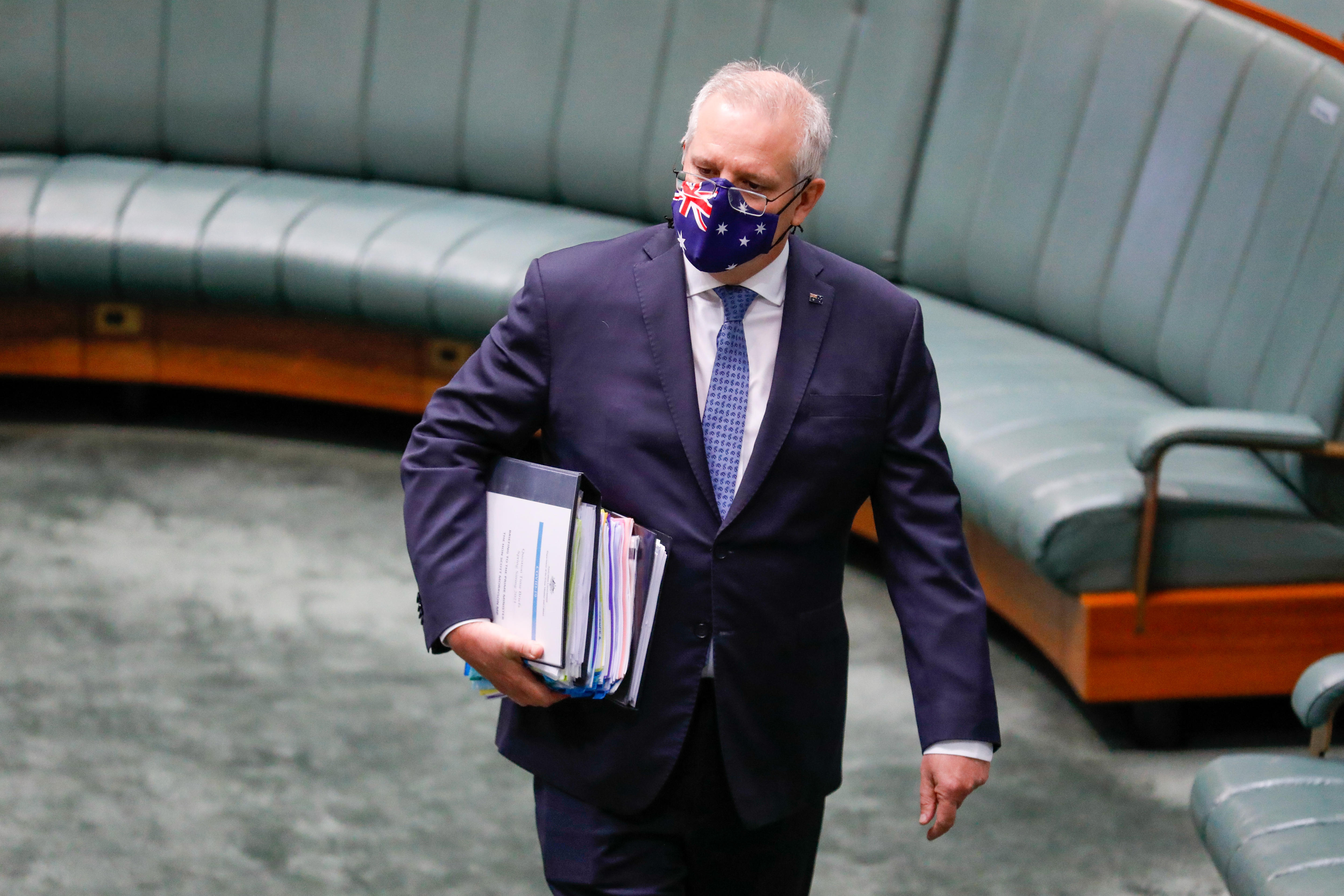 Morrison is wearing a mask with the Australian flag on it, holding binders, walking into chamber.