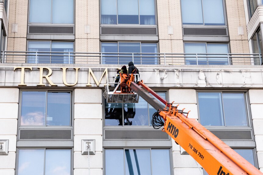 Two men remove the letters T.R.U.M.P one by one from the side of a building.