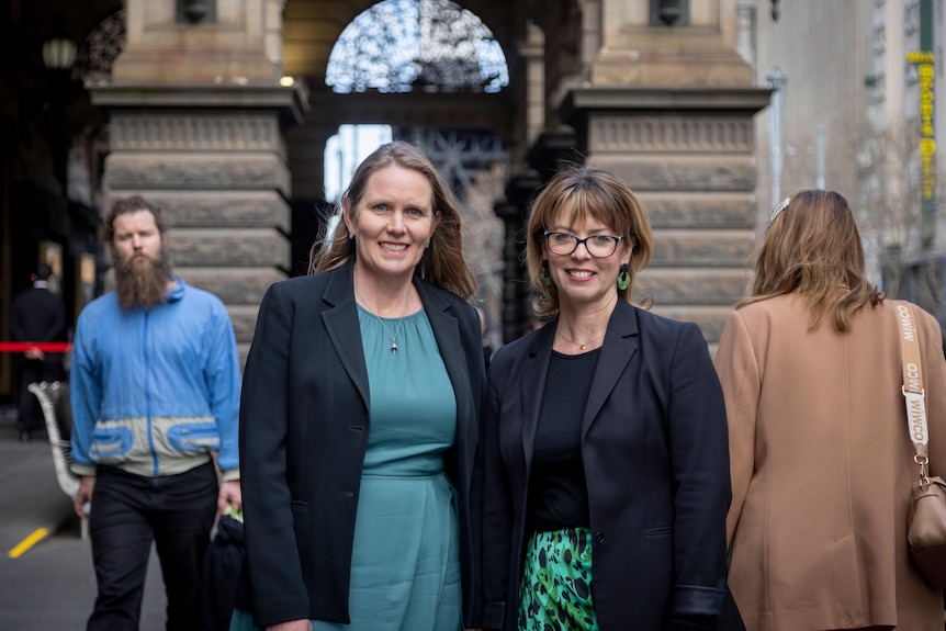 Two woman wearing black blazers stand together outside Melbourne Town Hall.