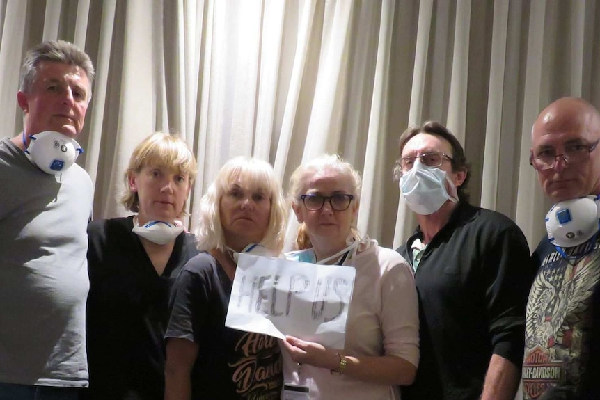 6 people wearing masks stand against a curtain holding a sign that reads "help us"