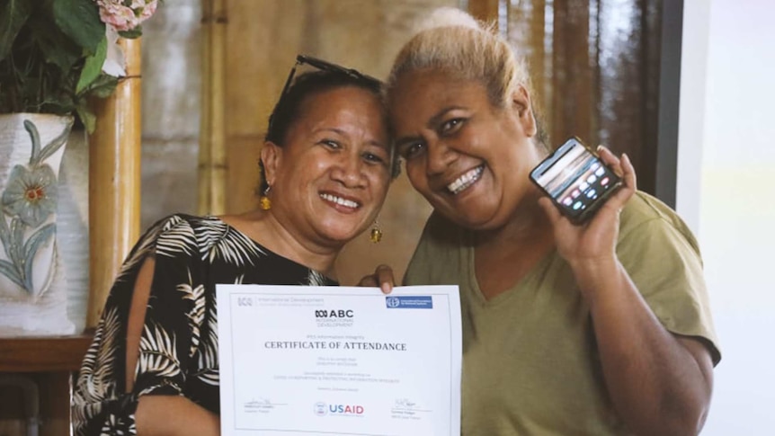 Two women hold the same Certificate of Attendance and one woman holds up a smartphone.