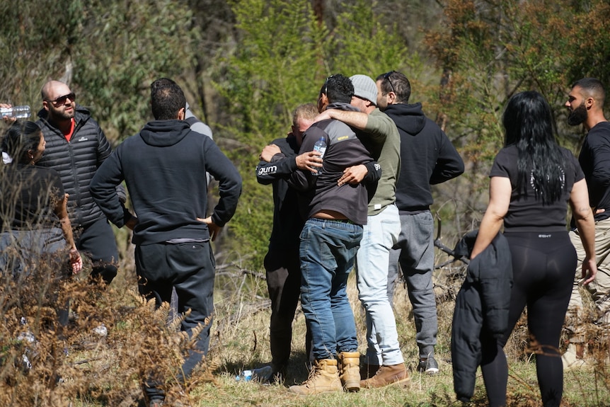 Men embrace as others look on.