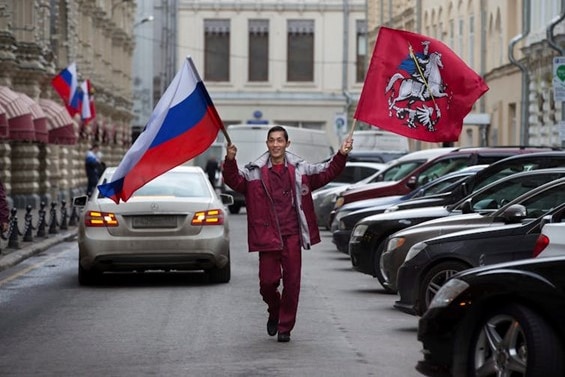 A Tajik migrant municipal worker carries Russian national and Moscow city flags in a street near Red Square in Moscow