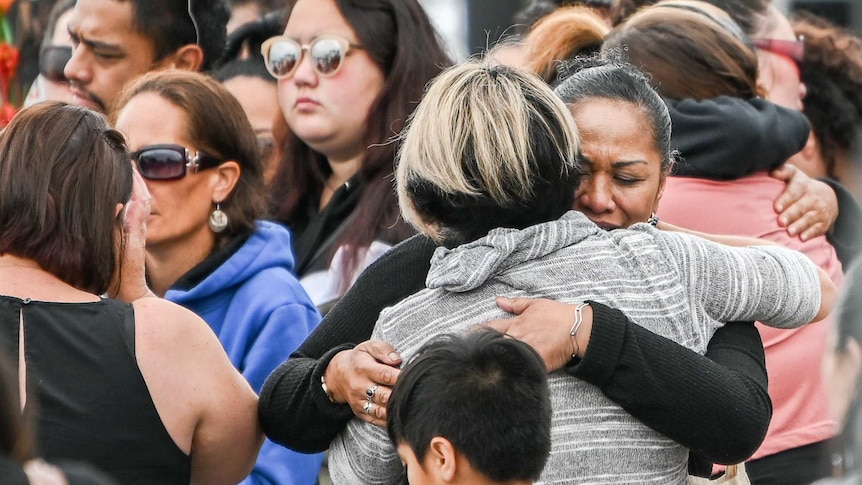 Two women embrace at centre of crowd, one is crying