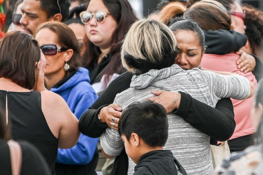 Two women embrace at centre of crowd, one is crying