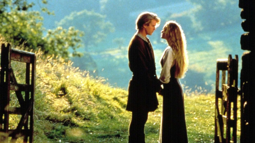 A man and a woman in medieval peasant dress stare lovingly at each other in front of a green landscape.
