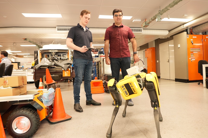 Two men stand with a robotic dog in a lab for a photo