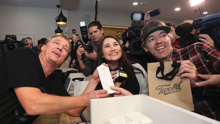 Three people pose with the receipt for the first legal recreational cannabis sold for use in canada.