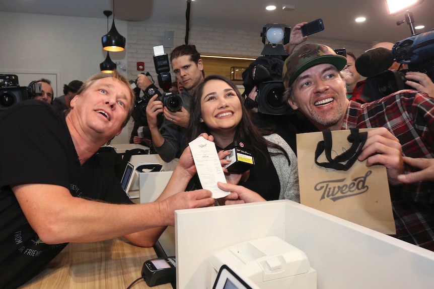 Three people pose with the receipt for the first legal recreational cannabis sold for use in canada.