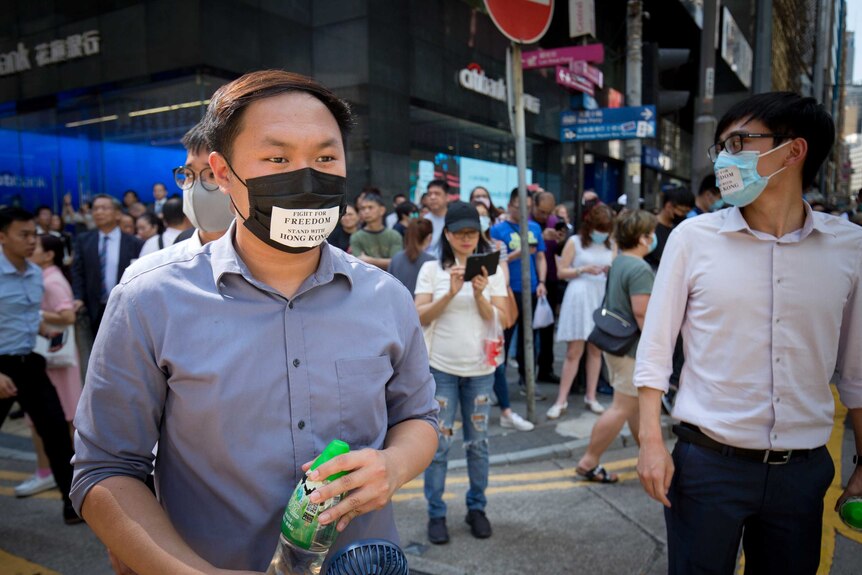 Hong Kong protesters stand with masks on that read "fight for freedom".