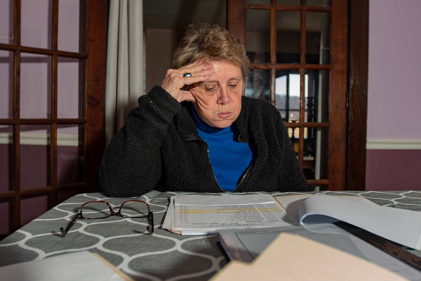 A woman sitting at a kitchen table looking at bills spread around her