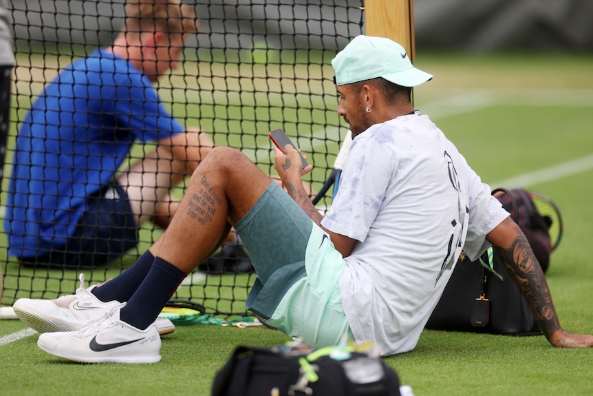 Nick Kyrgios sits on the ground looking at his phone  