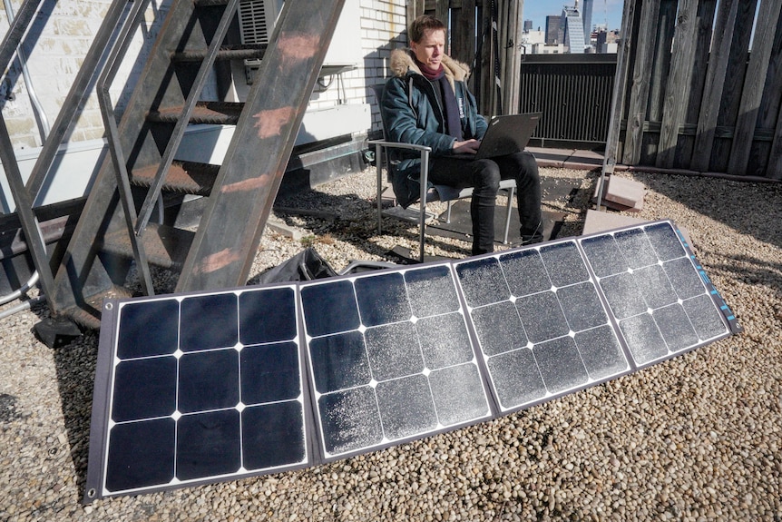 Josh Spodek sits and works on his laptop getting charged from a portable solar kit setup on the roof of his apartment