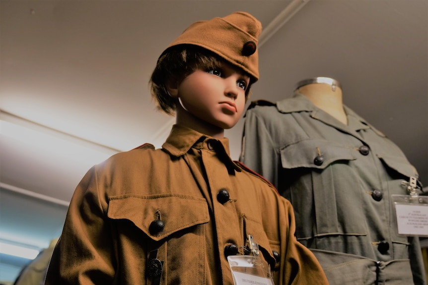 a male child mannequin stands dressed in a brown uniform and hat  