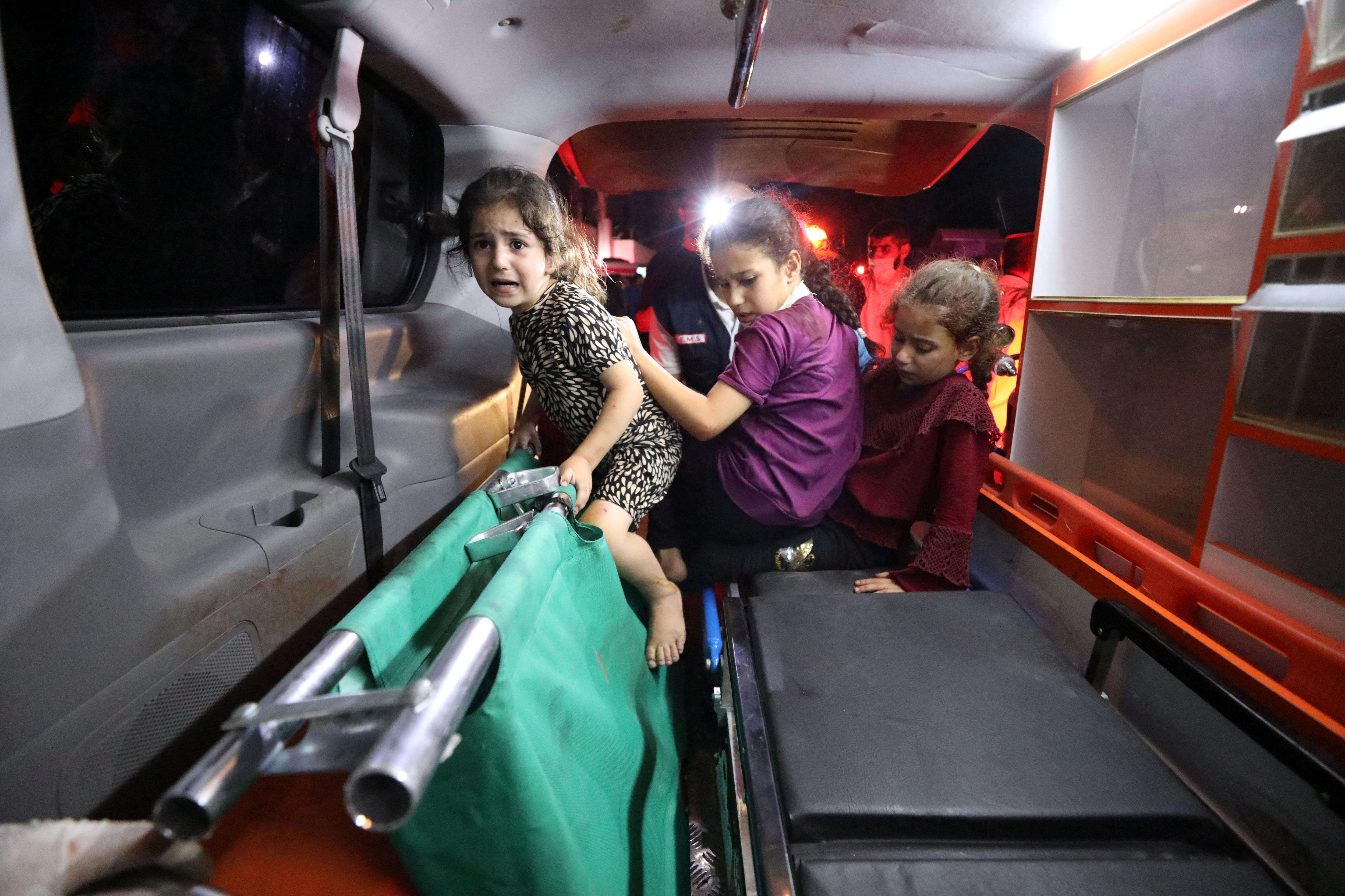 Three young girls sit in the back of an ambulance. They are visibly upset.
