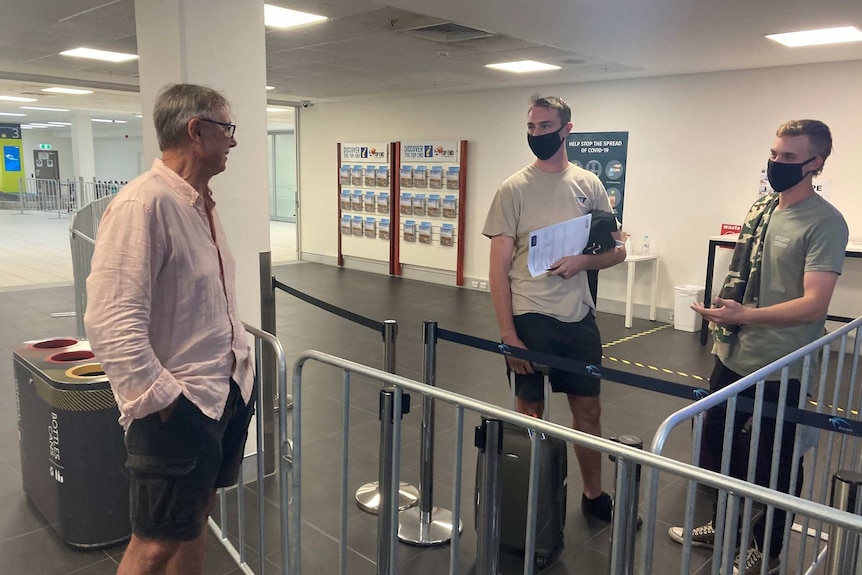 John Bonnin talks to his son Tom Bonnin across a barrier at Darwin Airport. Tom is standing next to another man wearing masks.