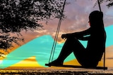 Silhouette of a woman on a swing that is hanging from a tree, with a sunset in the background