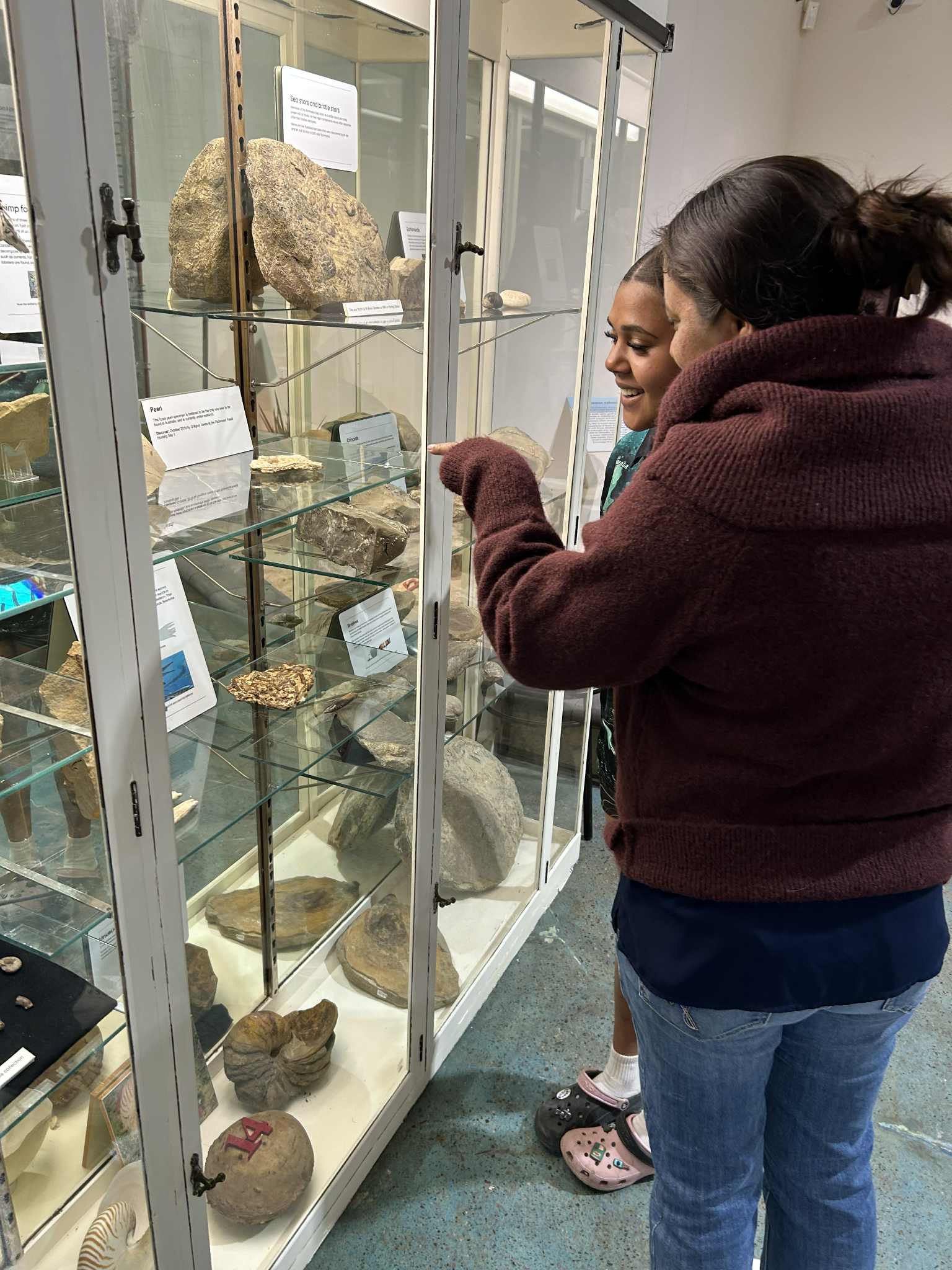 two woman point and smile at a fossil pearl in a glass case