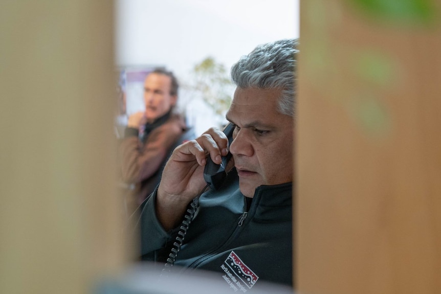 A man with silver hair looks concerned on the phone