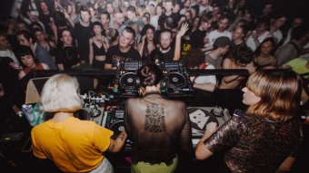 Three DJs mix music for a full mosh pit of clubbers.