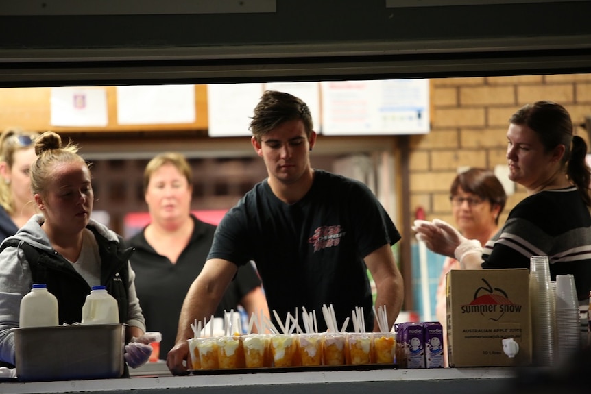 A young man prepares to carry a tray covered with deserts while others watch on.