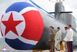 Military officials look at nuclear sub with red star on its front 