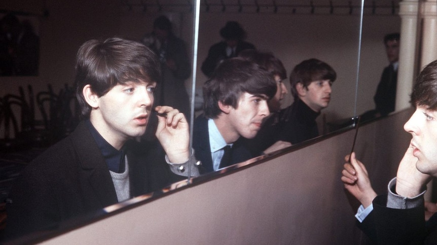 The members of The Beatles comb their hair in a mirror